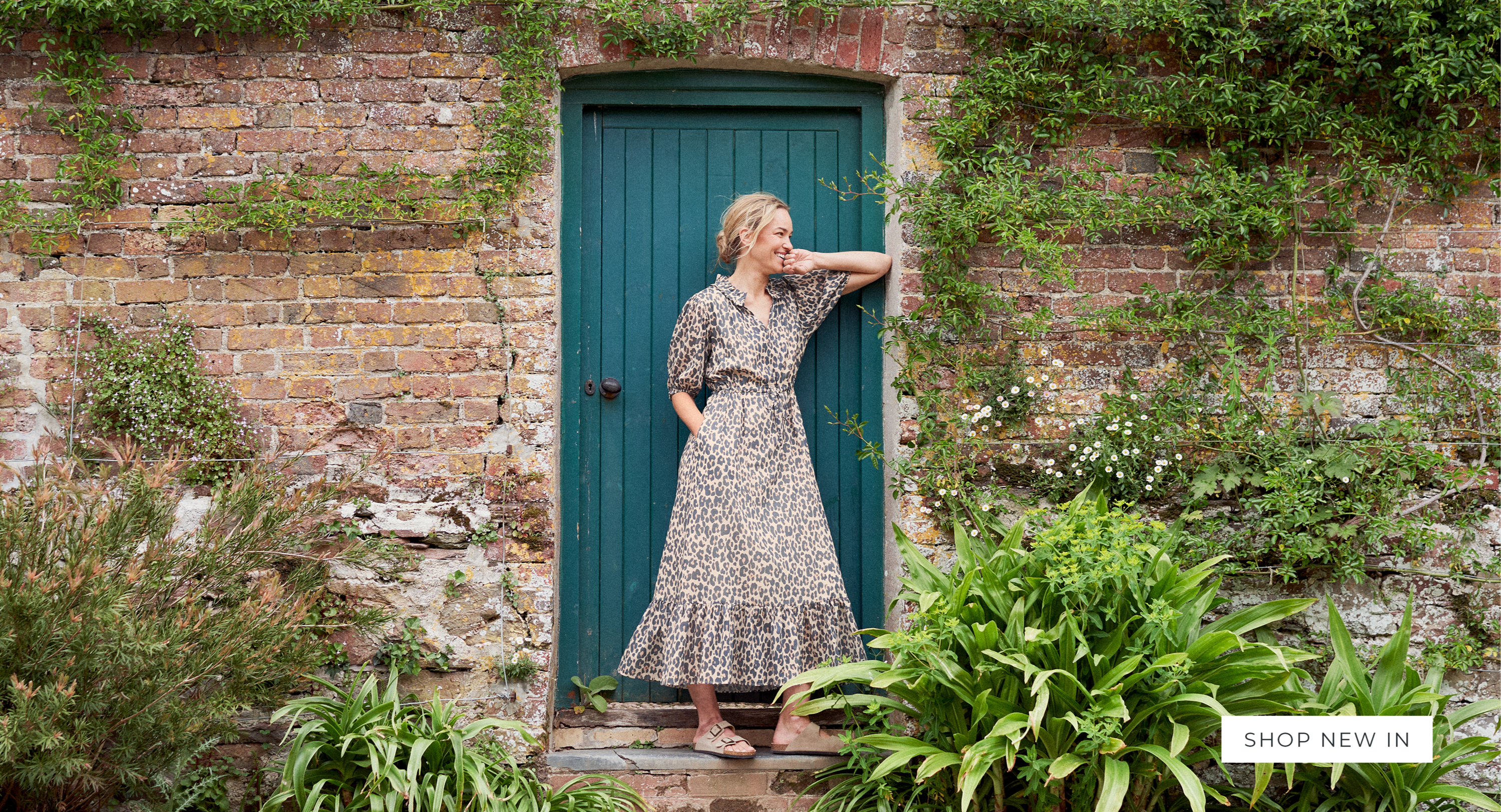Woman standing in a doorway in a garden wearing a leopard print midi dress