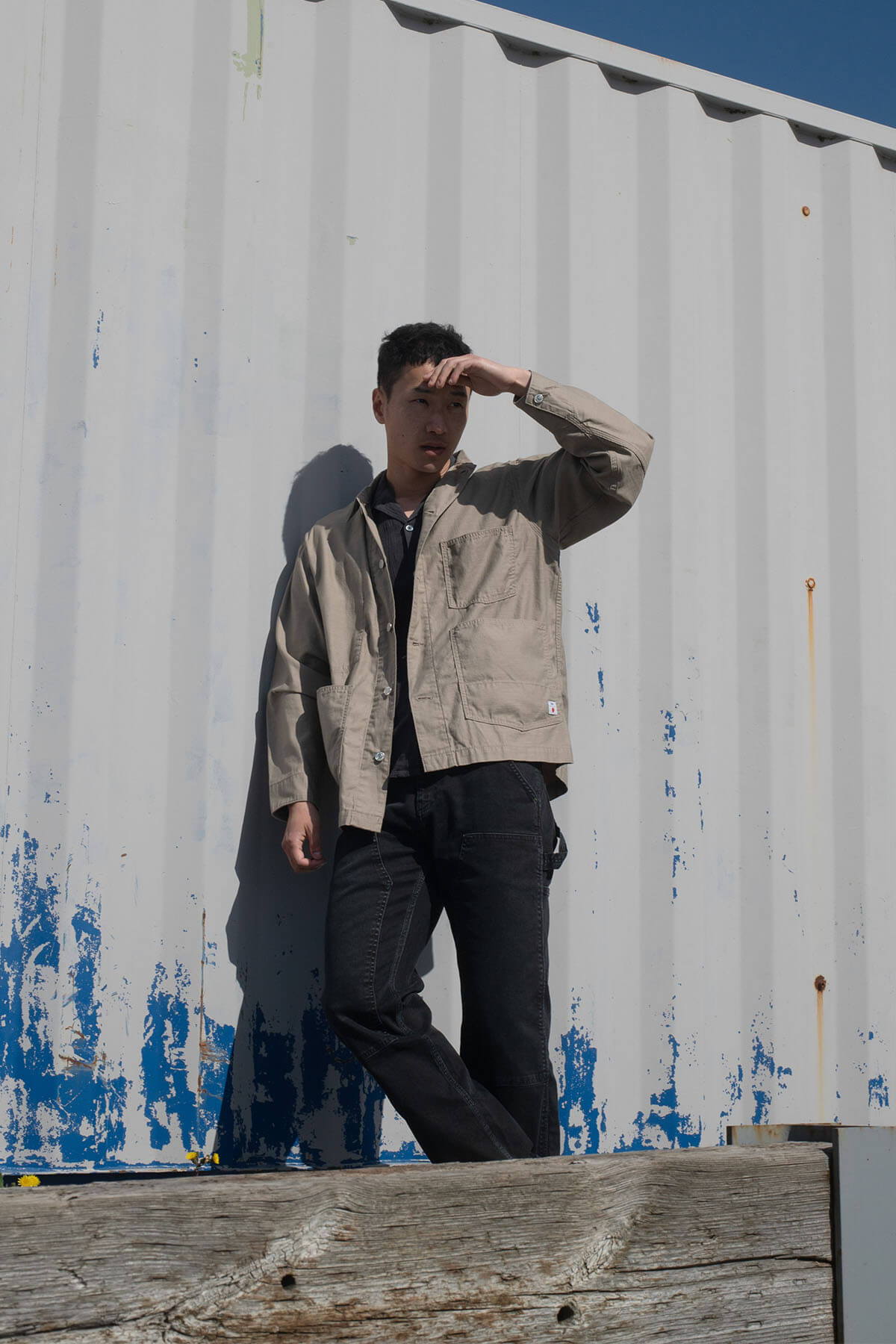 Person standing against a container, shielding eyes from sunlight.