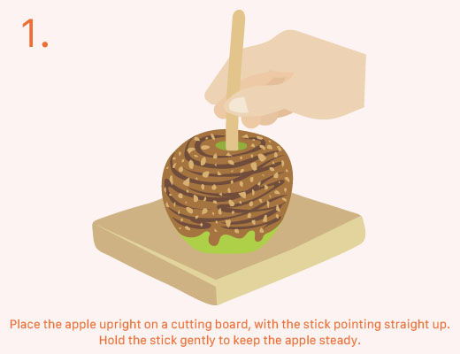 Hand placing a caramel-covered apple on a cutting board for preparation.