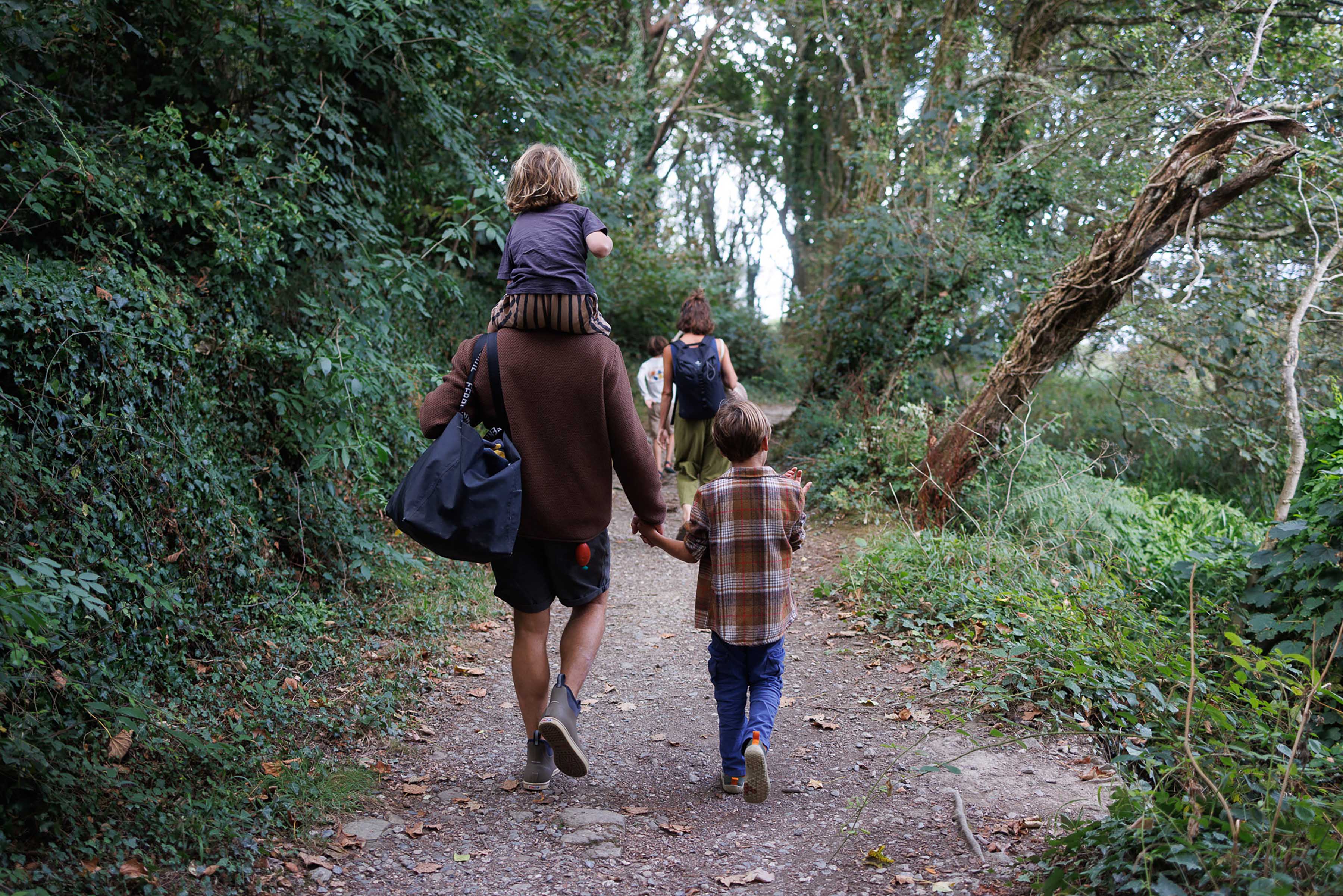 A family walking on a forest path, one child on shoulders.