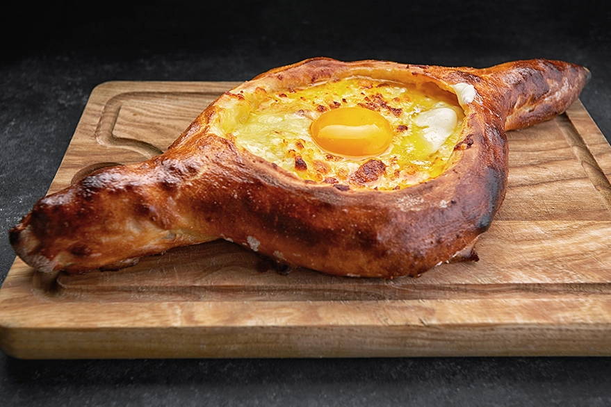 Adjarian khachapuri with molten cheese and an egg on a wooden board, a traditional Georgian cheese bread made with Suneli Valley Suluguni.
