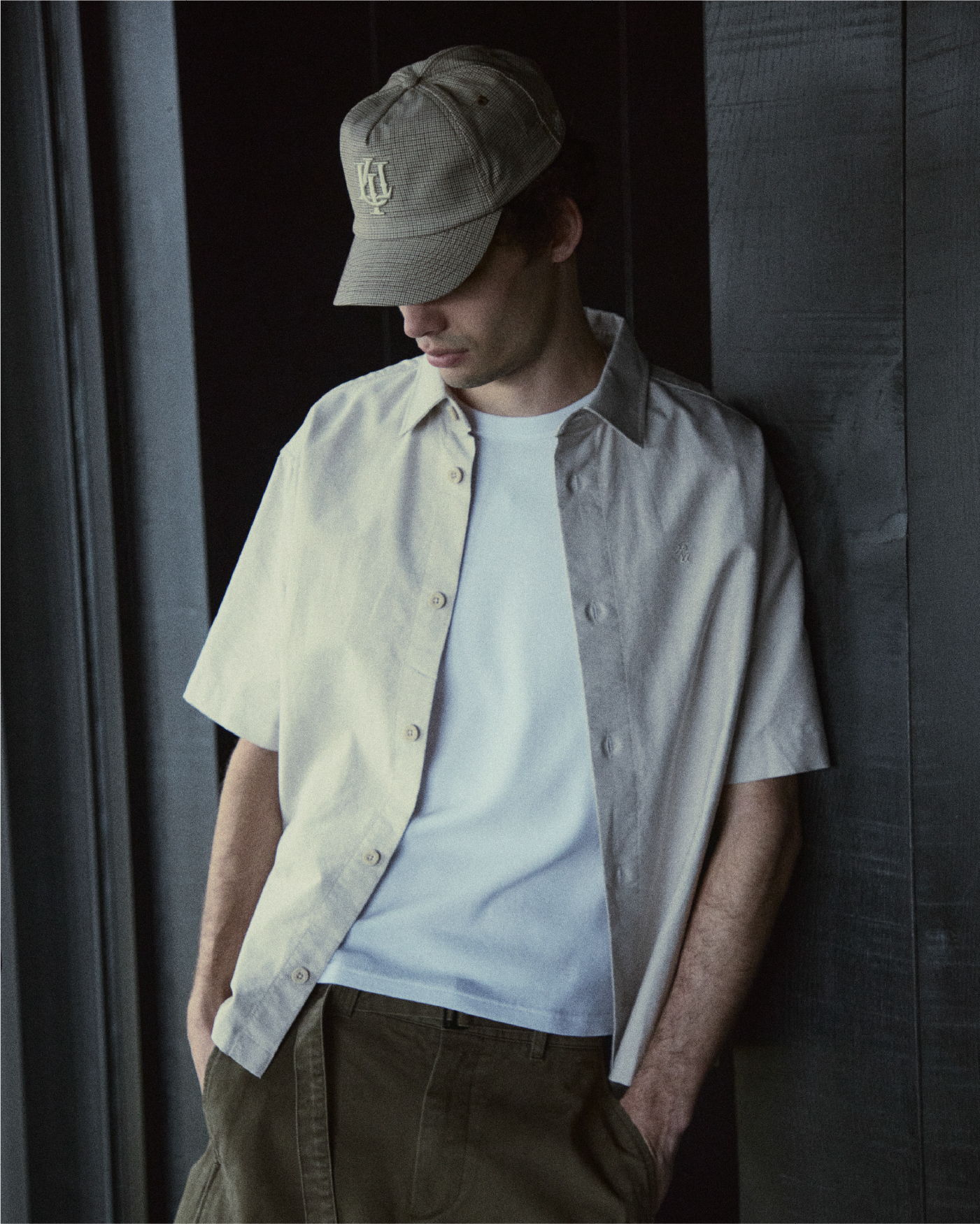 Young man in casual attire, standing against a dark wall.