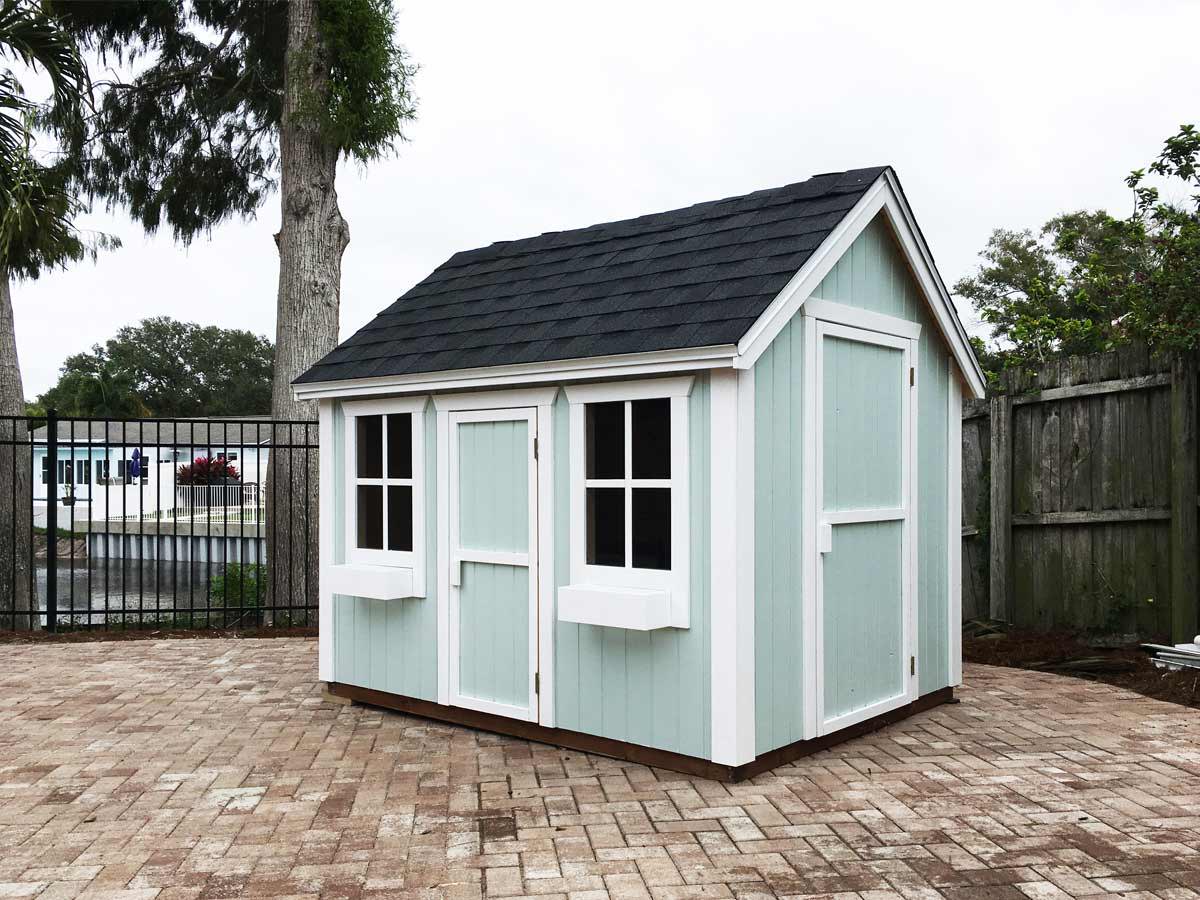 Light green custom playhouse in a garden with stone tiles by WholeWoodPlayhouses