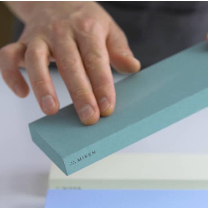 A chef rubbing the coarse surface of a green 220-grit Misen Sharpening Stone.