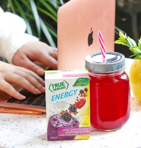 Someone at a laptop with a glass of True Lemon Energy Wild Blueberry Pomegranaate