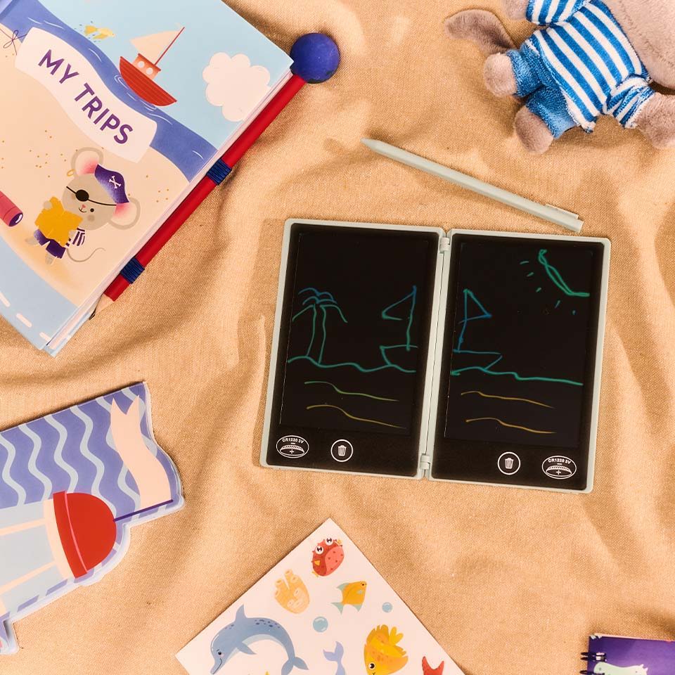 Colorful children's books and drawing boards on a sandy surface.
