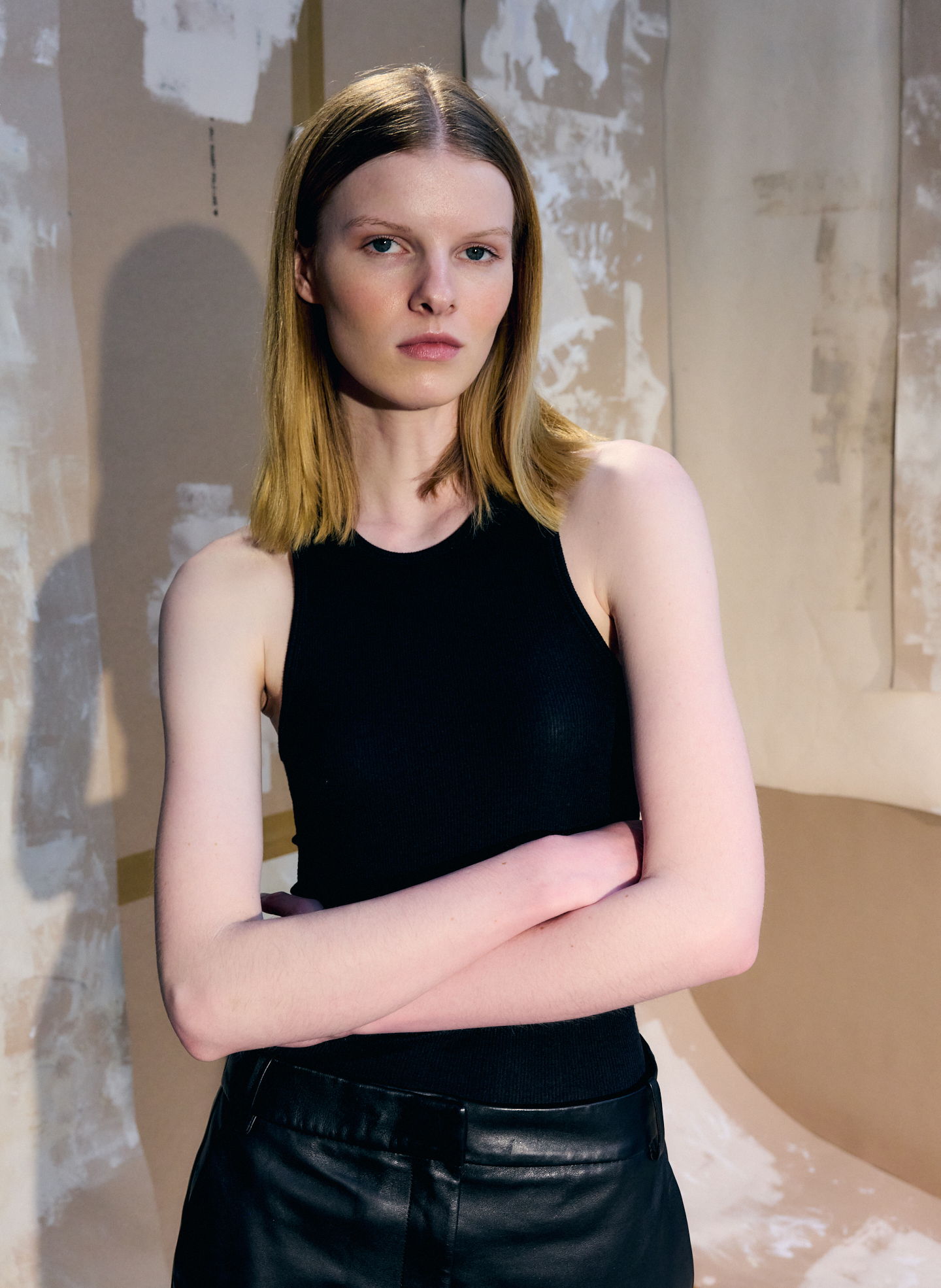 A model with straight hair wearing a black tank top and leather pants.