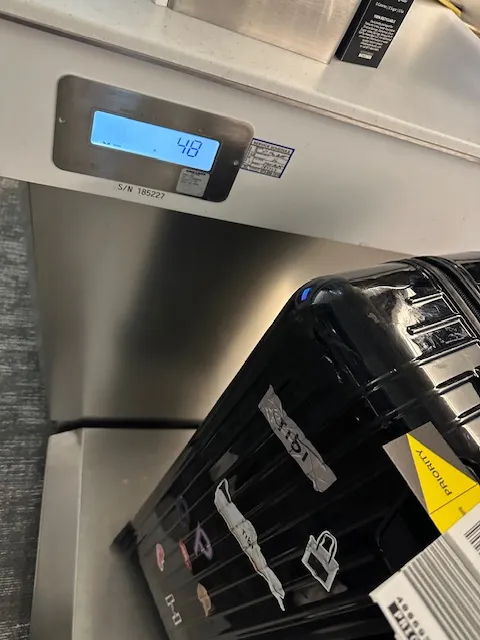 Digital scale displaying weight with a black suitcase nearby.