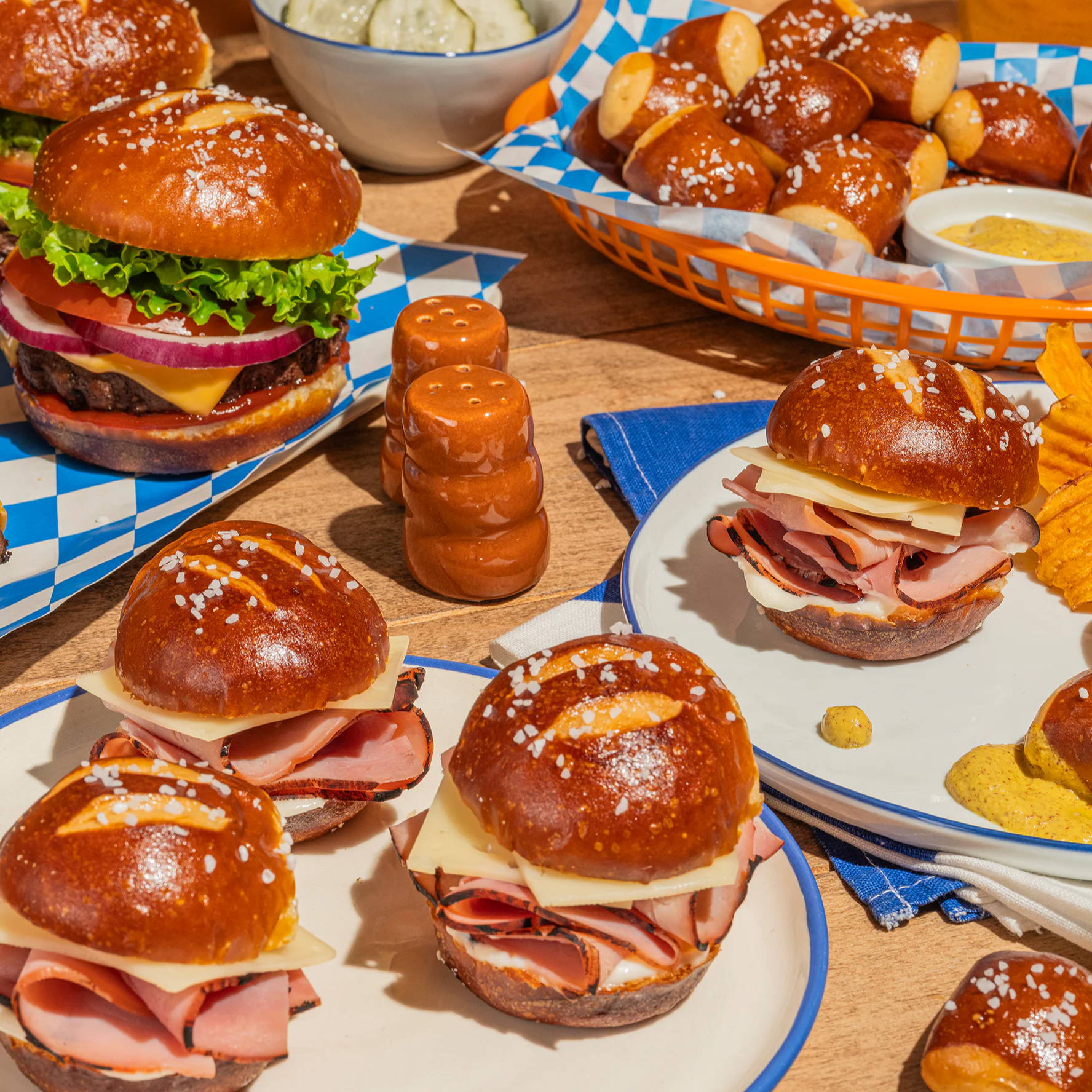 A variety of pretzel burgers and appetizers on a wooden table.