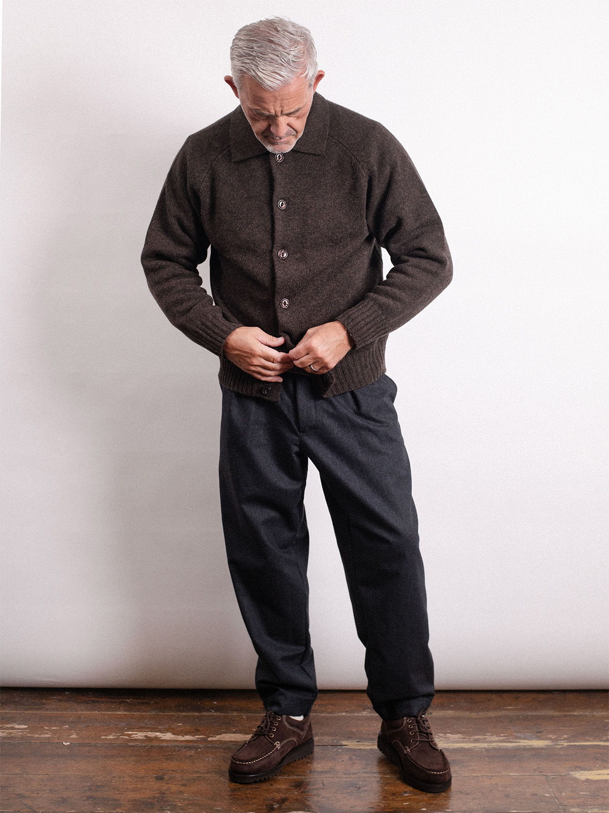 Rob buttoning a dark sweater, wearing dark pants and shoes.