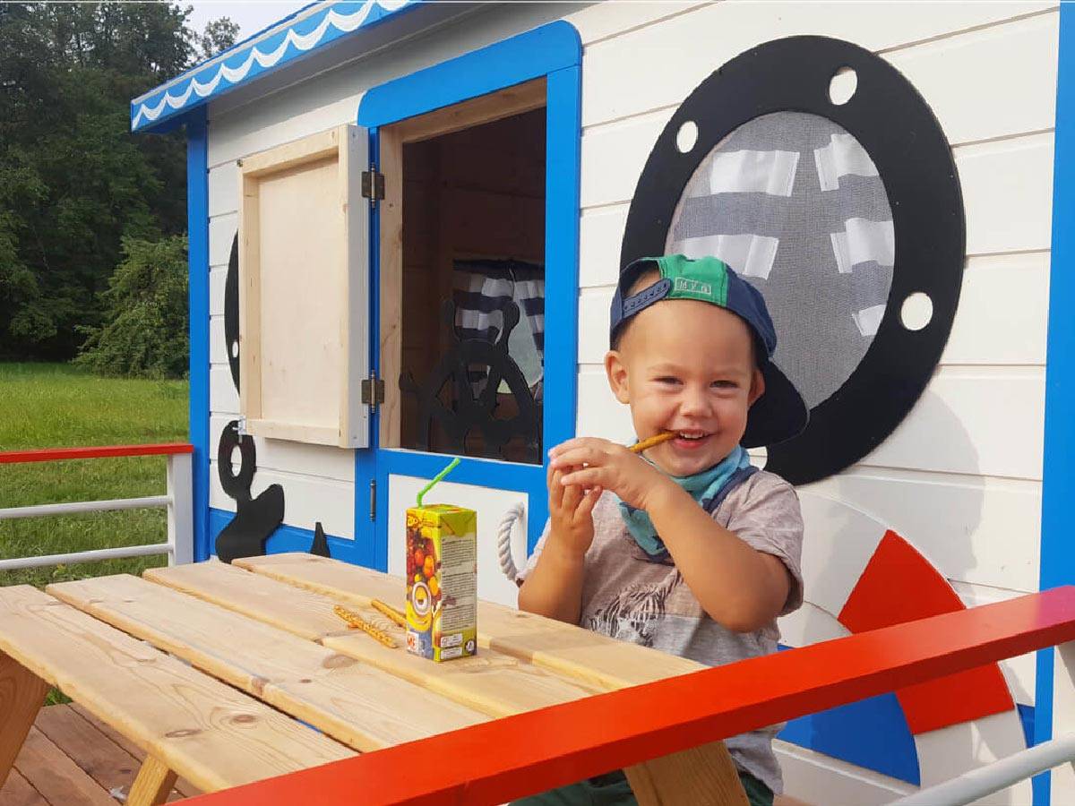 One boy eating on a wooden playhouse porch with forest on the background by WholeWoodPlayhouses