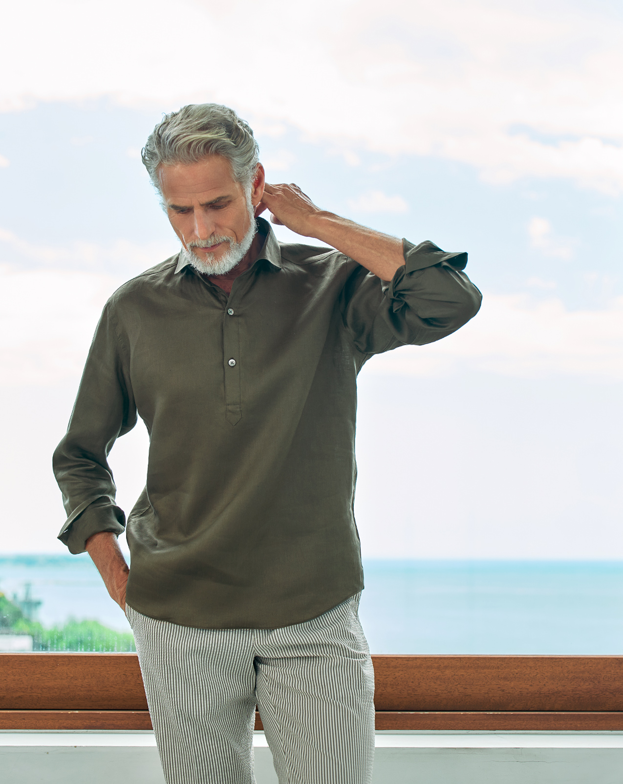 Man standing by a window, wearing a casual outfit with a scenic view.