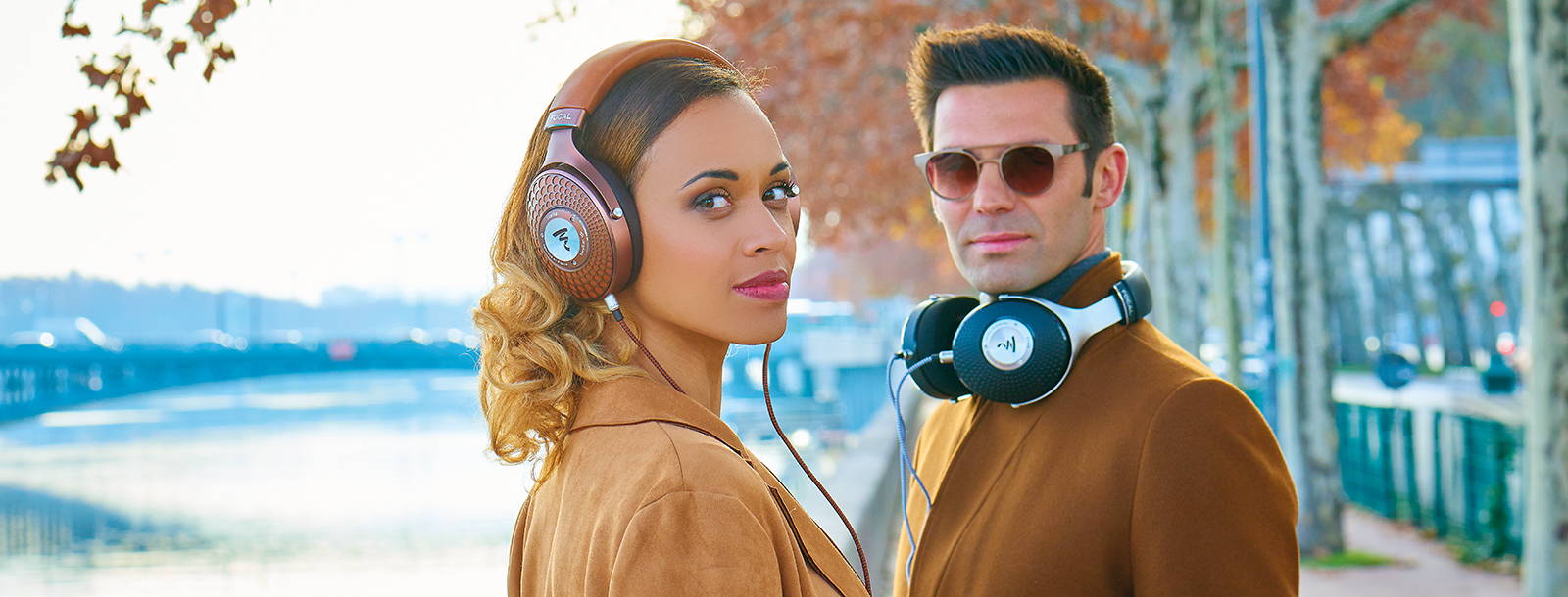 Photo of a well dressed woman and a gentleman posing with Focal Stellia and Focal Elegia closed back headphones.
