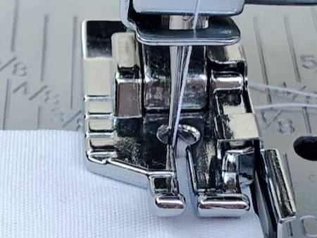 detail of the quarter inch quilting foot with guide on a sewing machine and a white piece of fabric