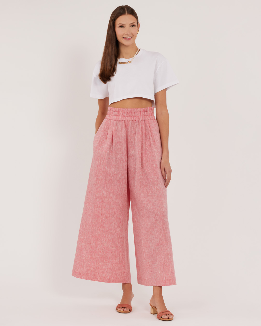 A woman wearing a cropped white top and pink wide-leg pants.