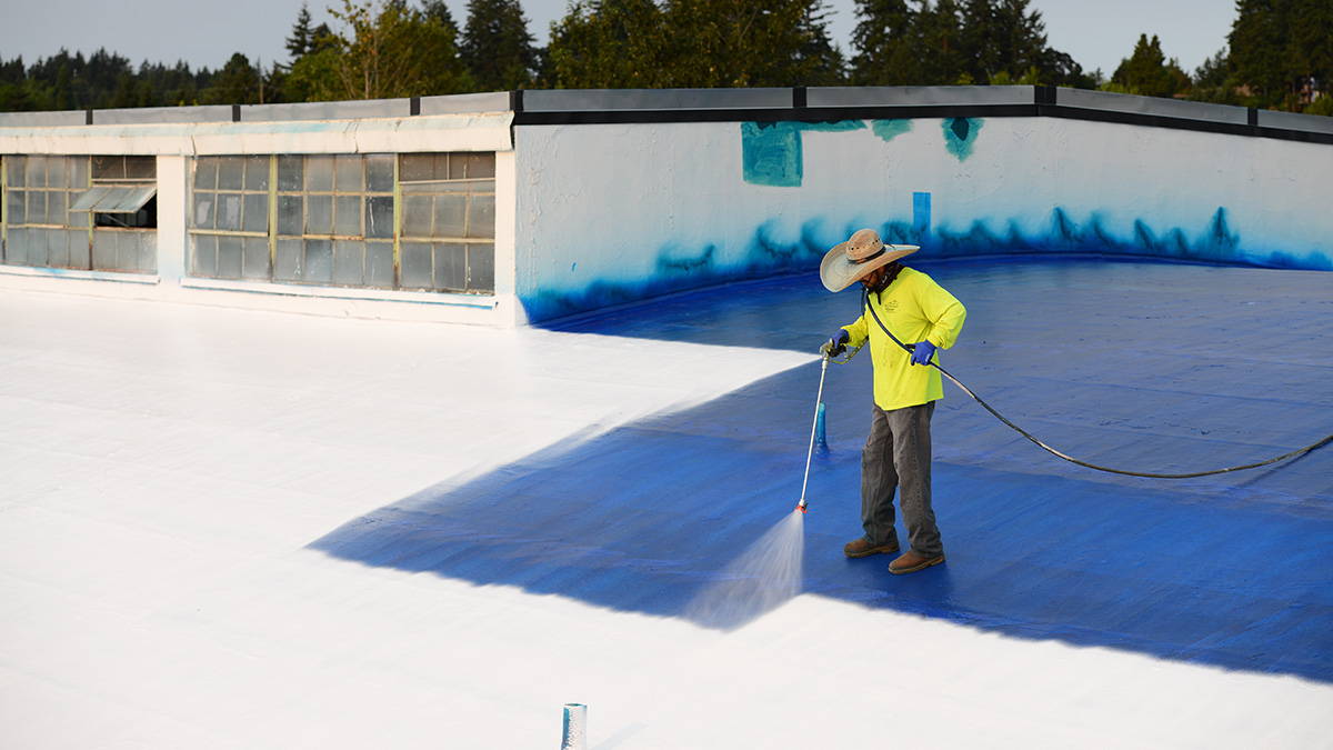 Man using sprayer to apply elastomeric roof coating.
