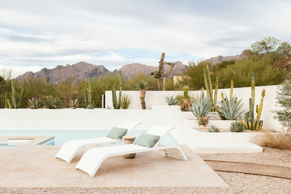 Two white chaise loungers with sage pillows in a desert climate pool area.