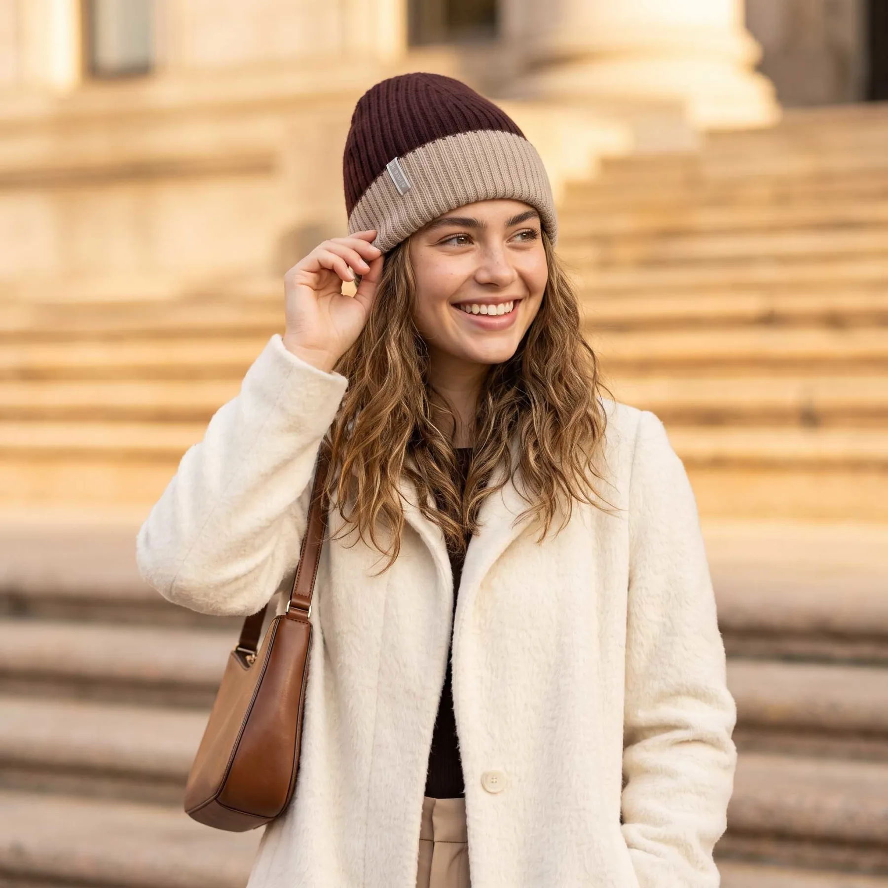 Smiling woman in a coat and beanie stands on steps.