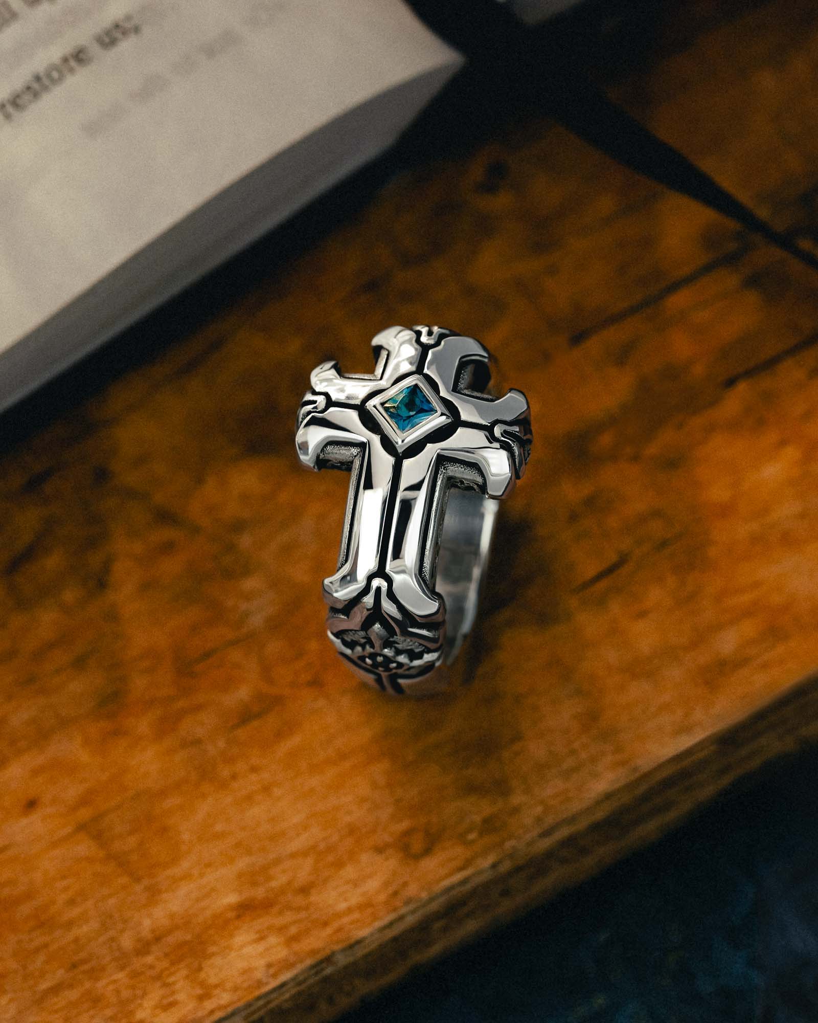 Silver cross ring with a blue gemstone on a wooden surface.