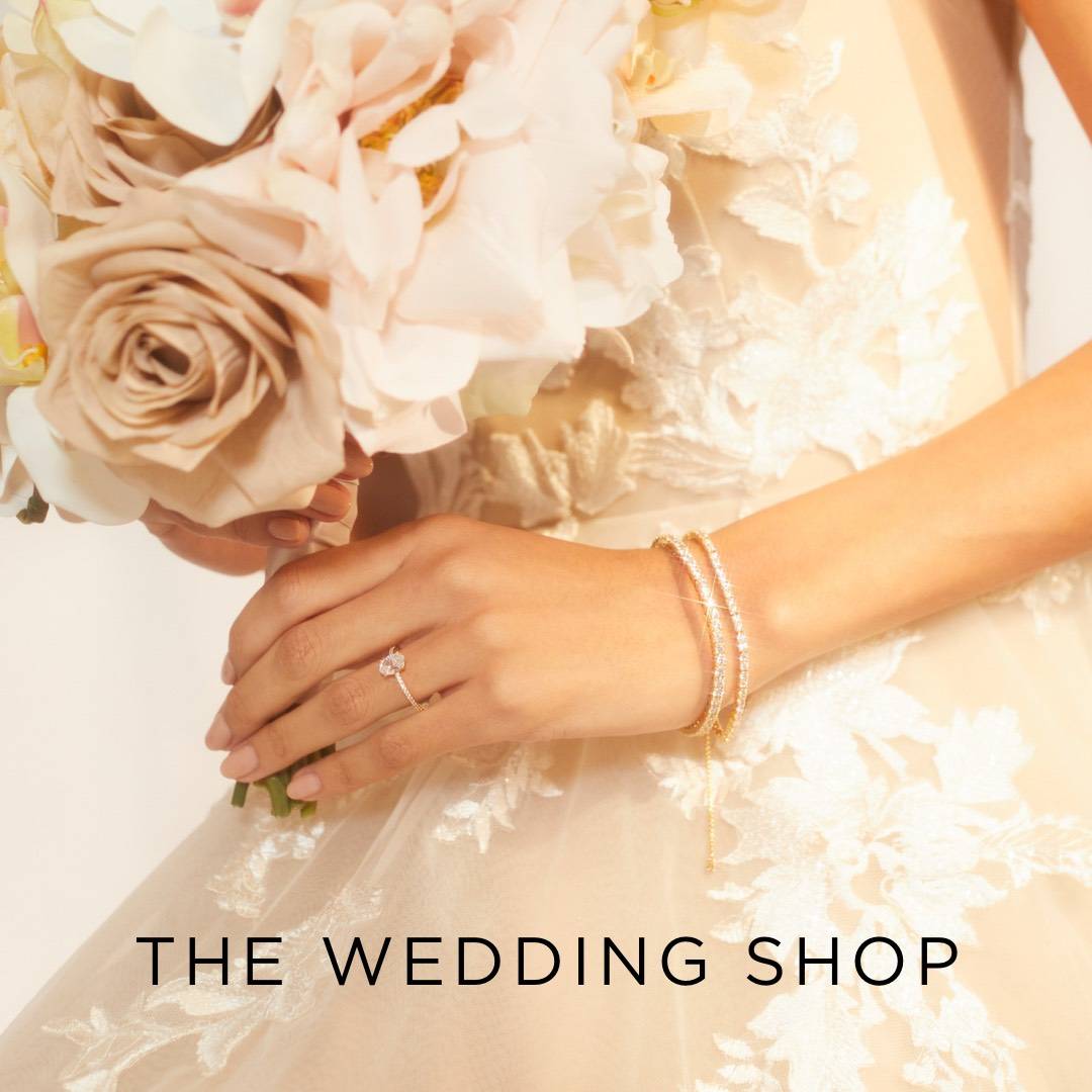The Wedding Shop.  Image of a bride's hand holding a bouquet and wearing an oval solitaire CZ ring and two CZ tennis bracelets. 