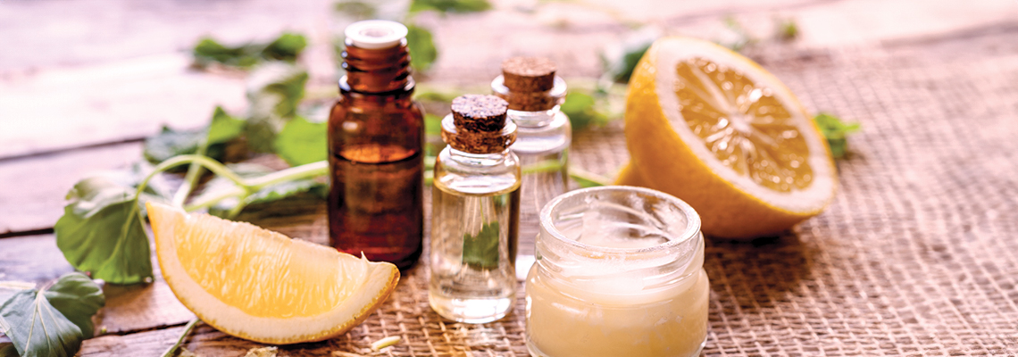 Bottles of essential oils, lemon slices, and a cream on a wooden surface.