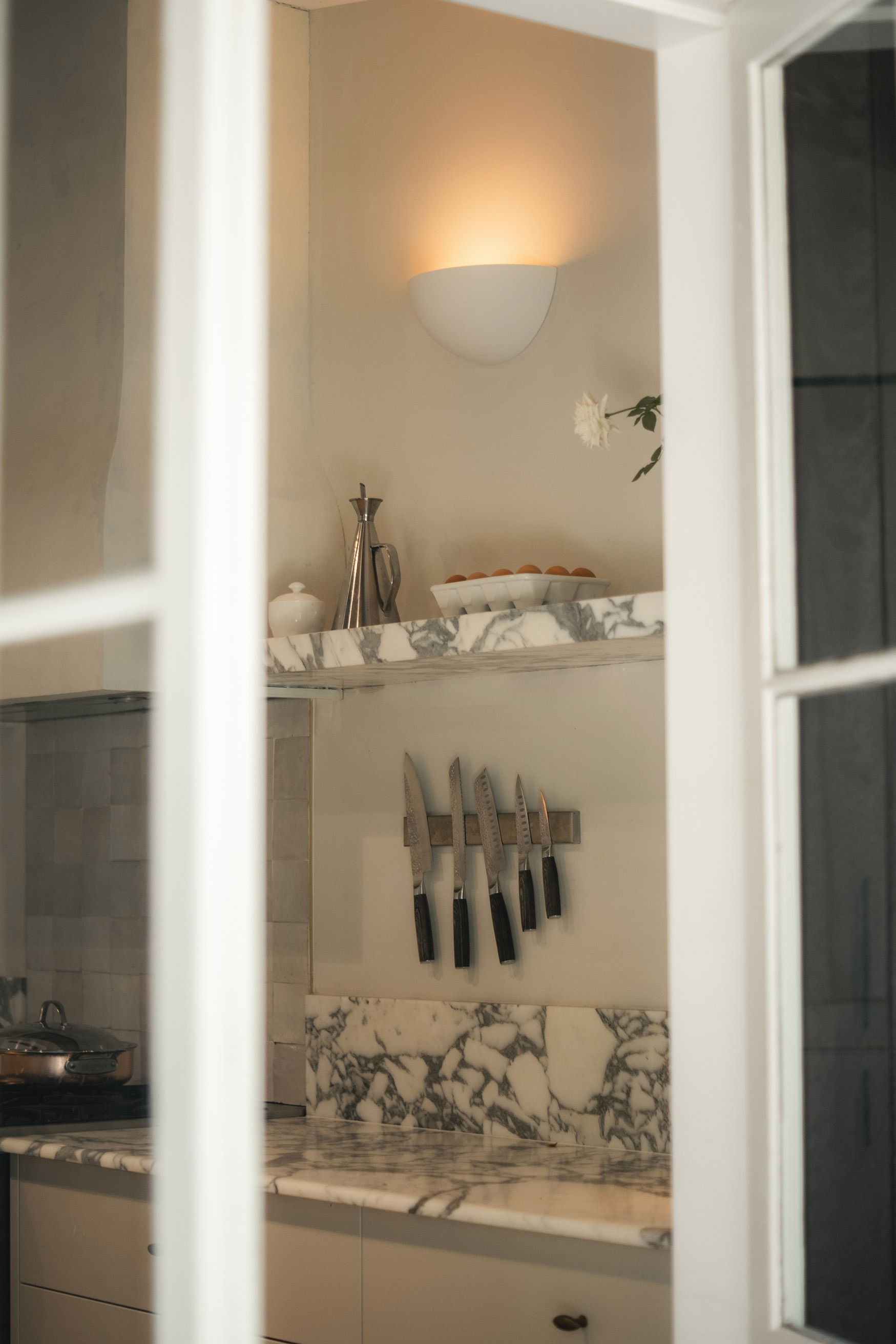 View of a modern kitchen through a window, featuring marble countertops and a knife rack.