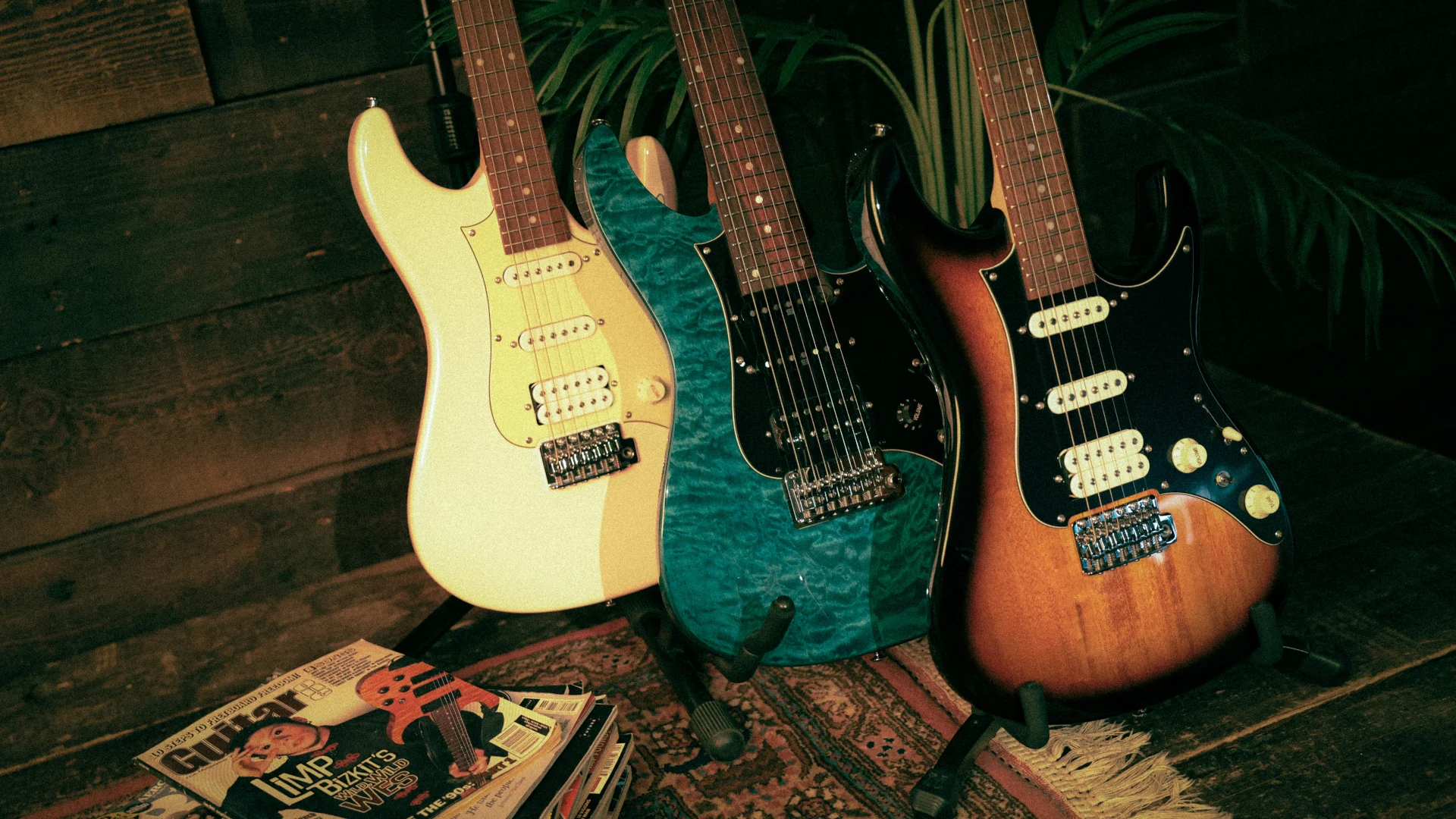 Three Ibanez AZ Series electric guitars leaning against a wooden backdrop with vinyl records.