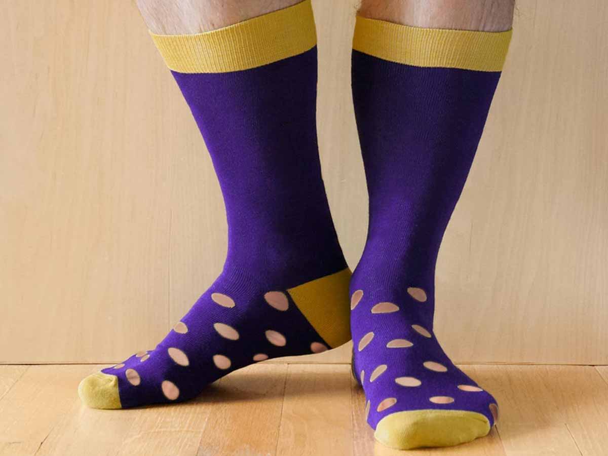 Men's feet wearing purple and gold socks with holes in the bottom
