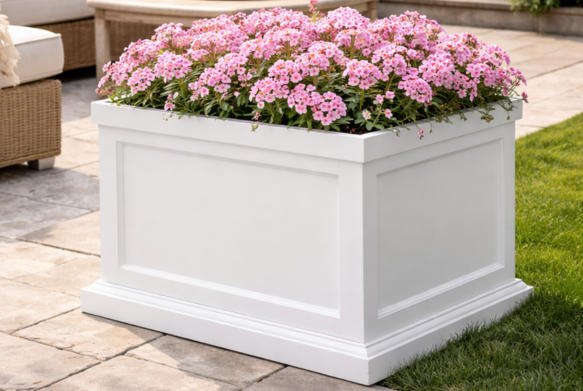 White planter box filled with pink flowers on a patio.