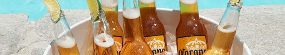 A bucket of beer bottles on a sandy surface near water.
