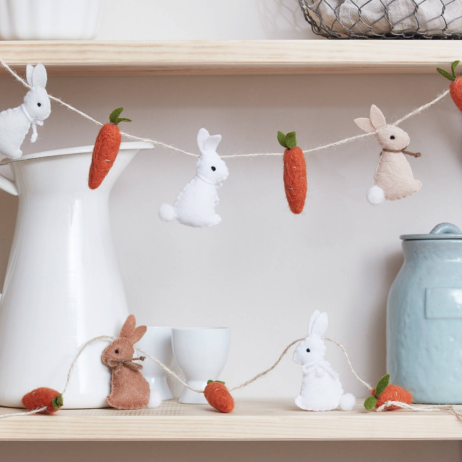 White and brown felt rabbits on a garland with cotton carrots on an Easter shelf.