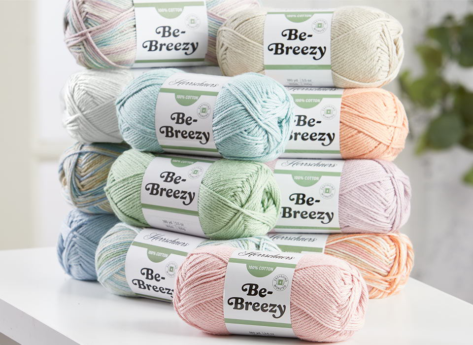 A stack of Herrschners Be-Breezy, colorful yarn balls, with labels reading 
