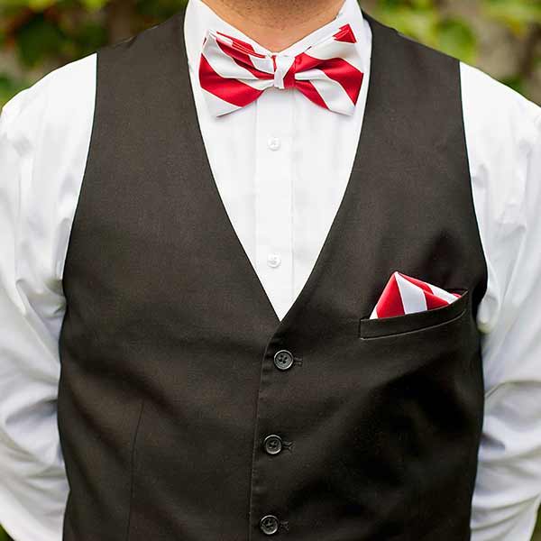 Man wearing a red and white striped bow tie and pocket square with a black uniform vest