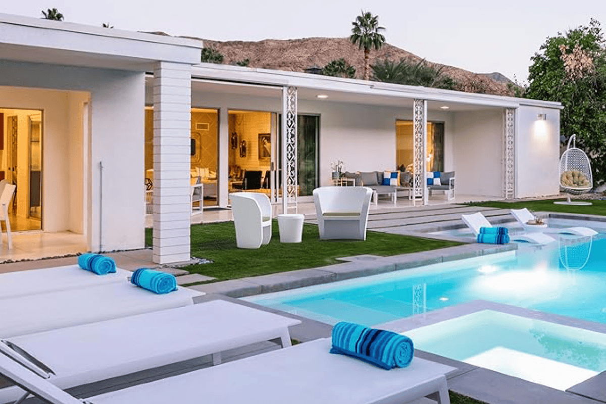 Modern home with a pool featuring in-pool chaise loungers on a tanning ledge, plus poolside seating and towels arranged on a spacious deck.