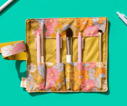 Pictured is our Tootsie Roll product, a roll-up pouch with slots to hold pens, makeup brushes, paintbrushes, and more. This particular one has a pattern of green, pink, orange, and blue wildflowers flowers. 