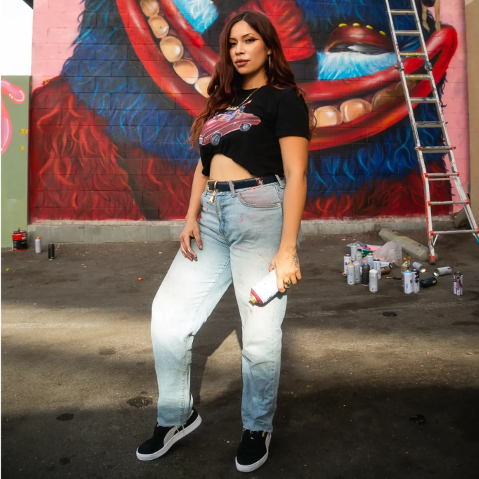 woman holding spray paint in front of mural wearing puma suede shoes