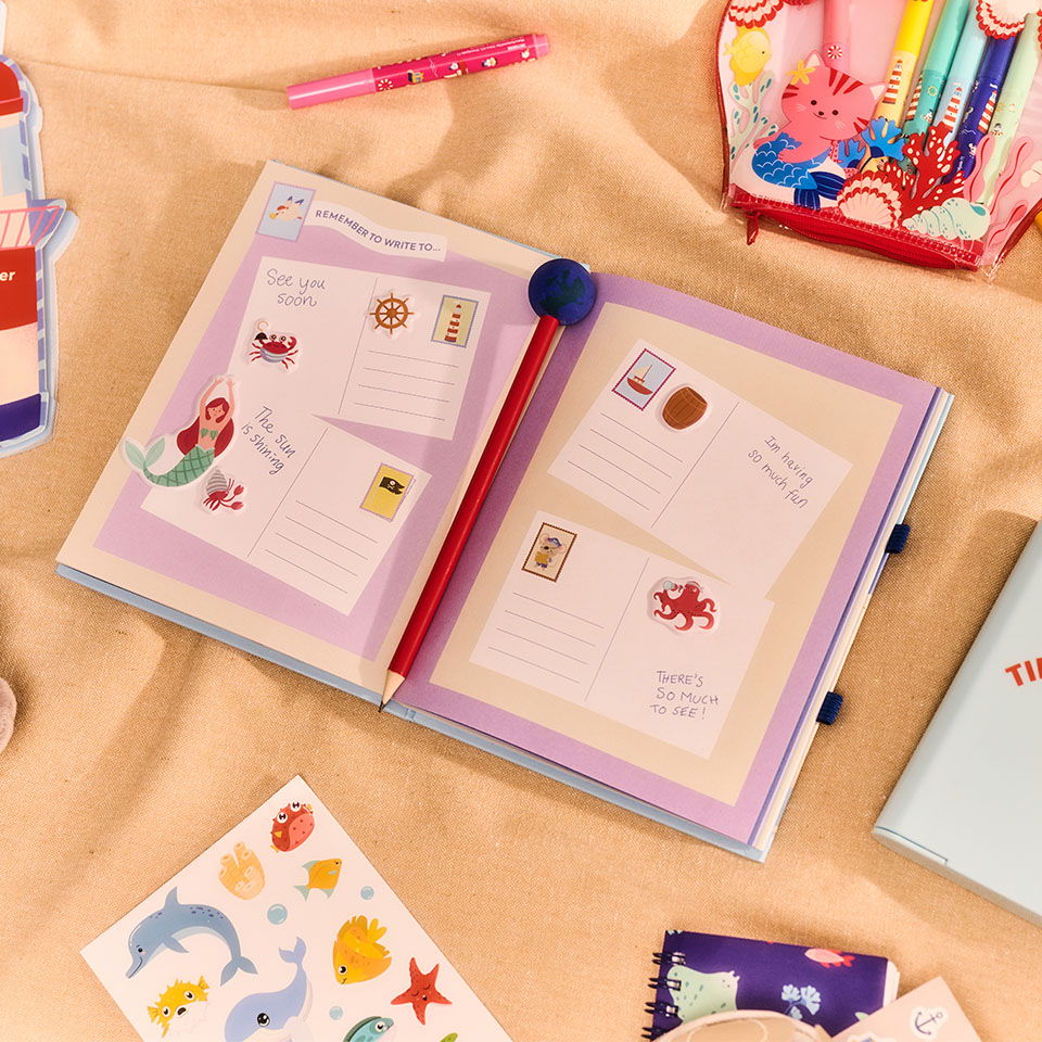 Open scrapbook with colorful stickers and postcards on a soft surface.
