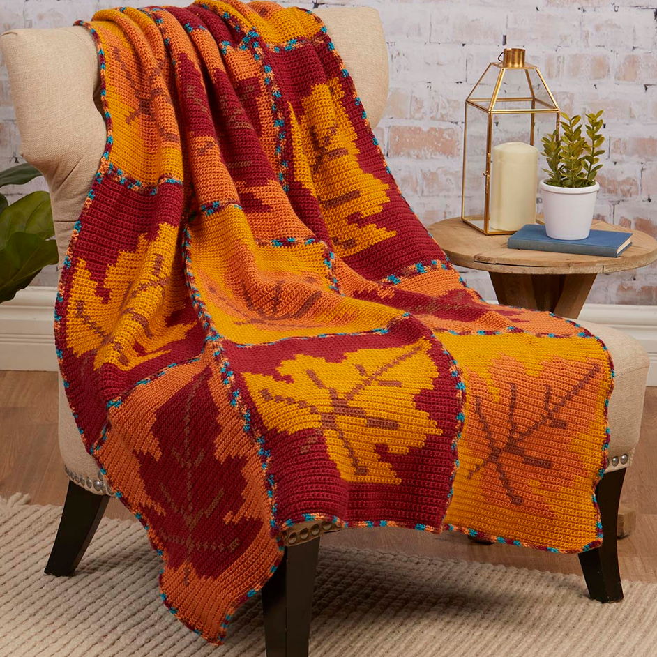 Colorful leaf-patterned blanket in shades of orange draped over a chair.