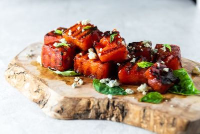 Grilled watermelon cubes topped with herbs on a wooden serving board.