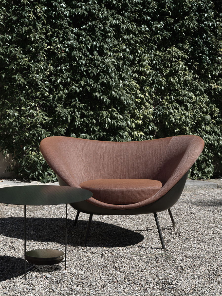 Modern chair and side table in a gravel outdoor setting with greenery.