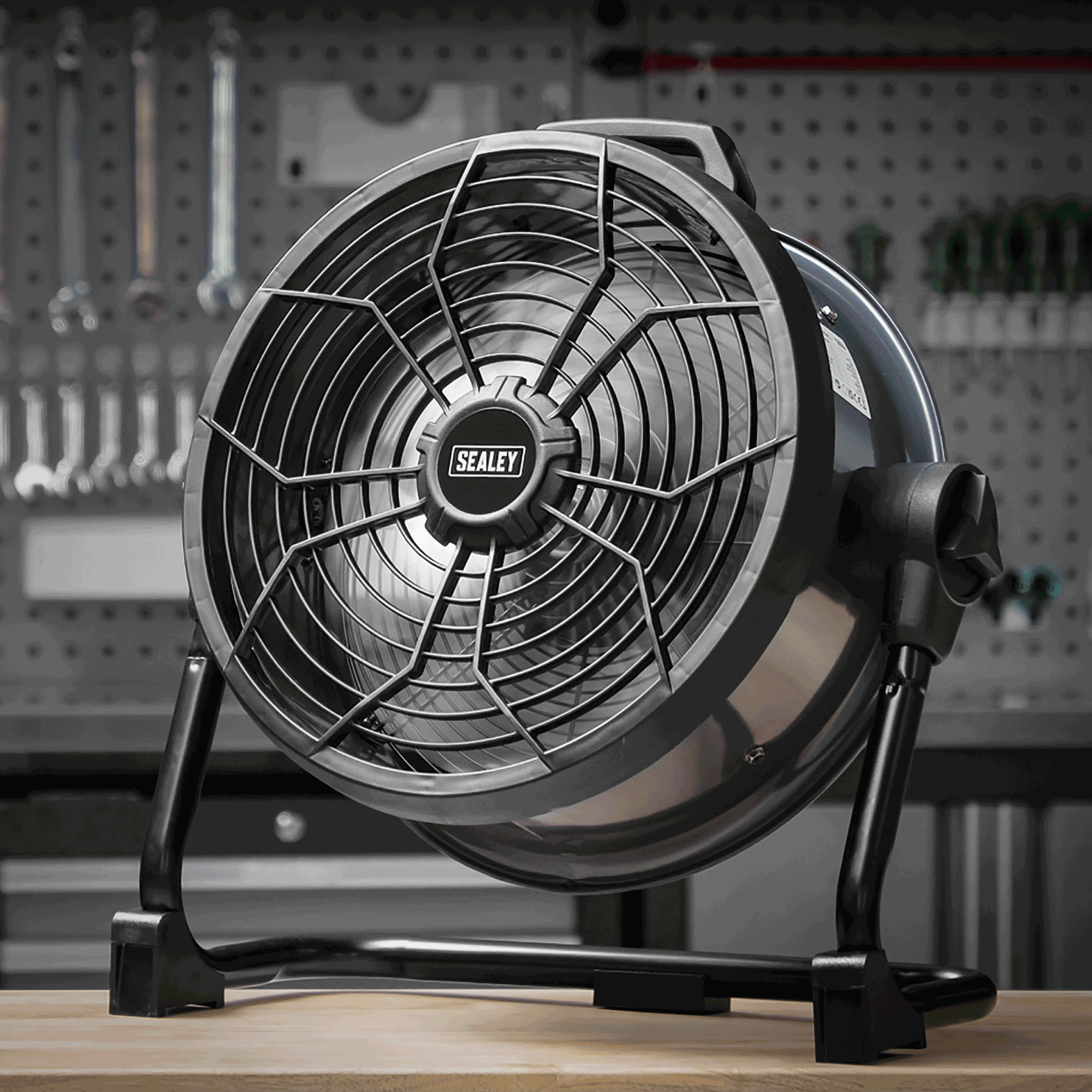 A black fan on a workbench with tools in the background.