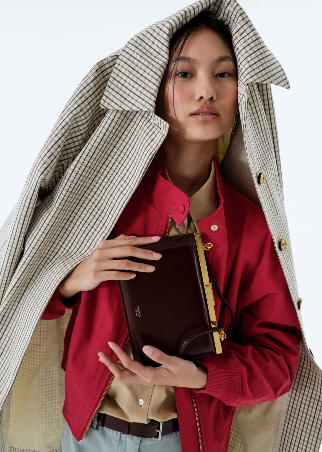 A person in a red jacket holding a notebook, covered by a coat.