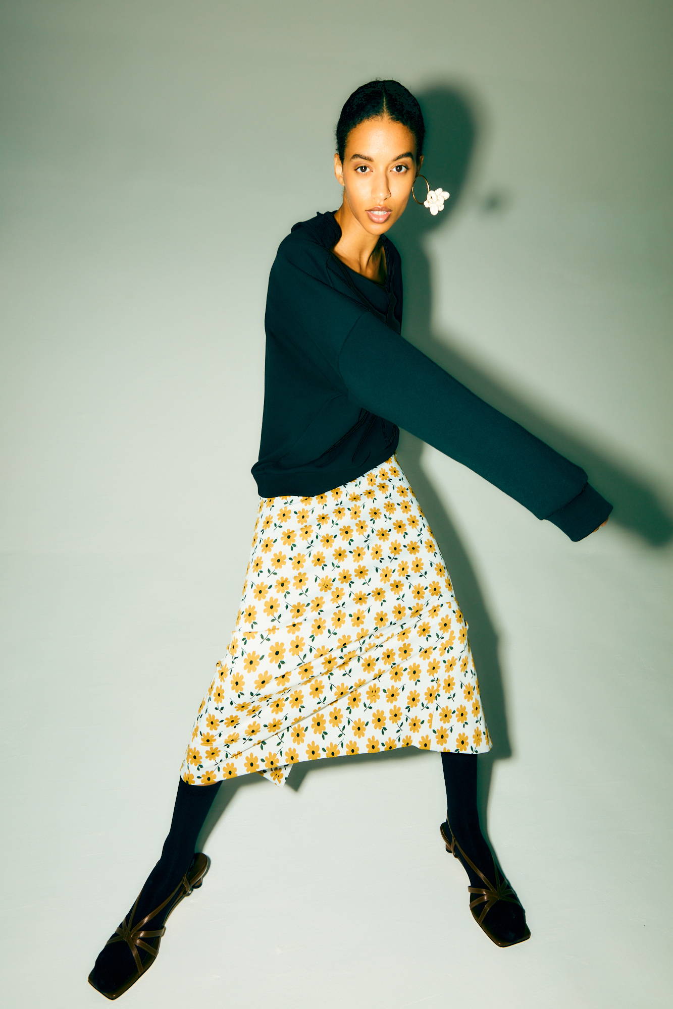 Model in a floral skirt and sweater, striking a dynamic pose.
