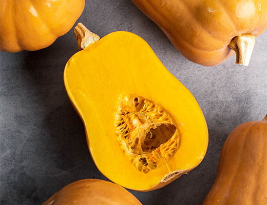 A halved butternut squash surrounded by whole squash on a gray surface.