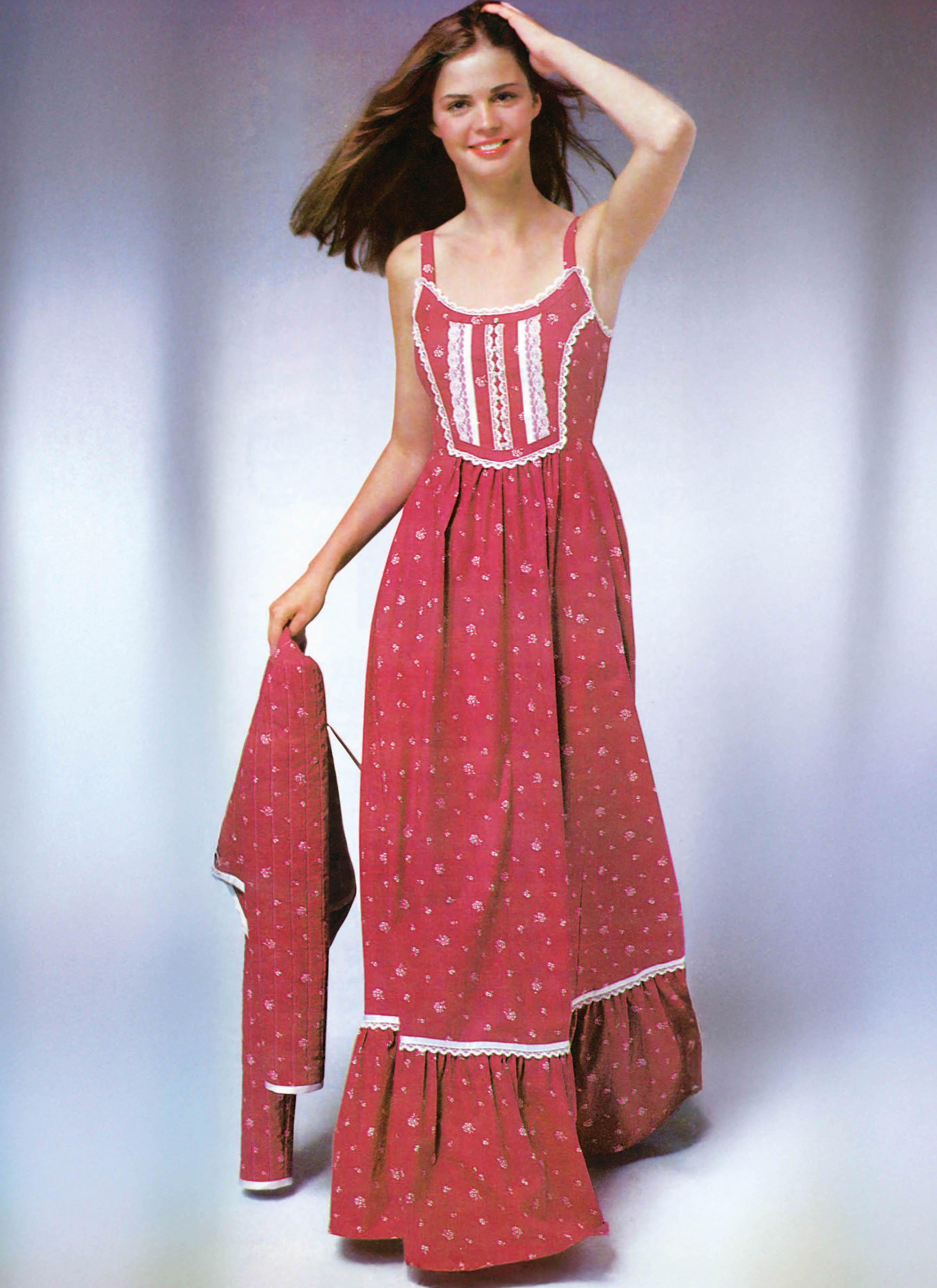 A woman wearing a long, red floral dress with spaghetti straps.