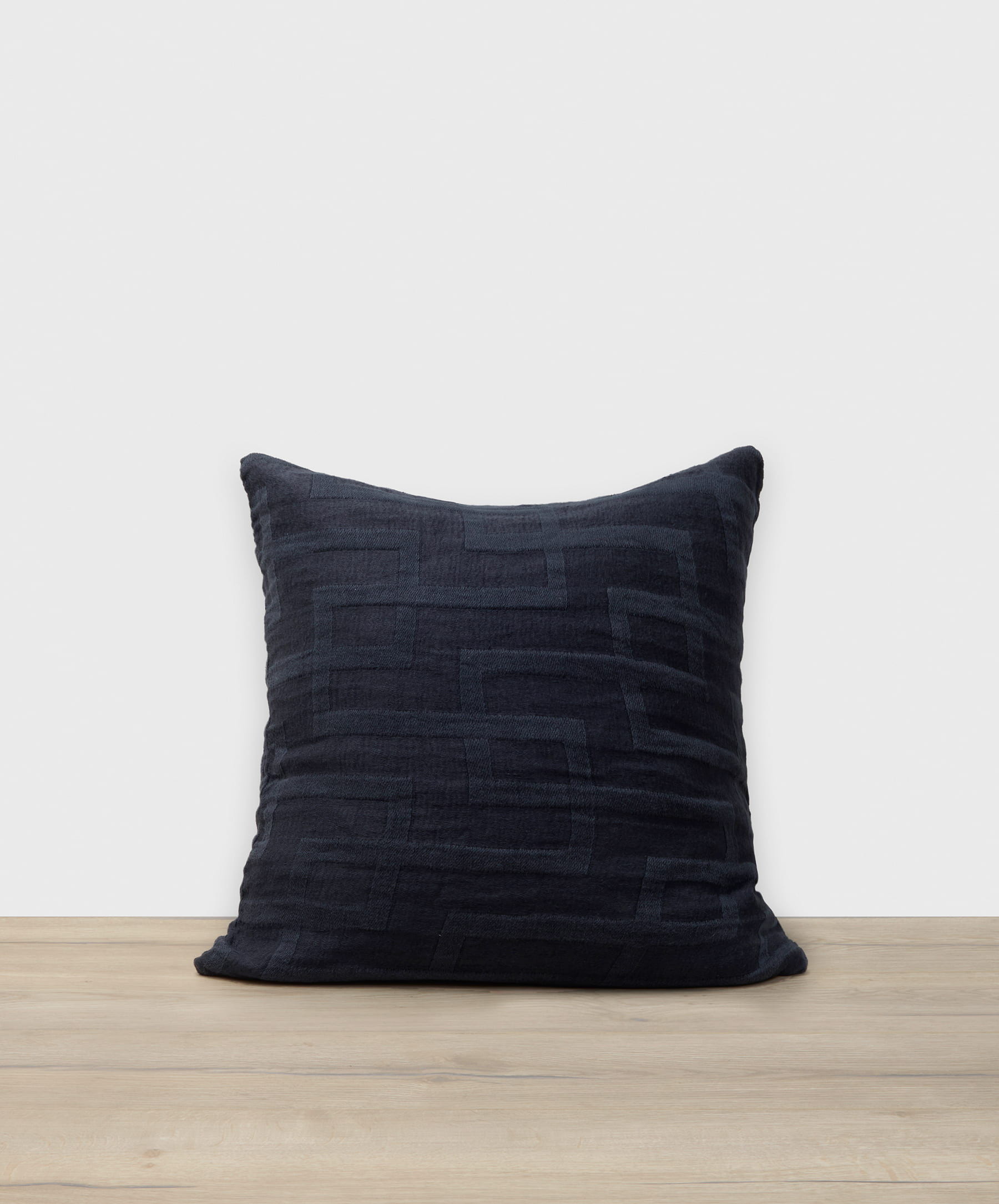 Dark blue textured pillow on a wooden surface with a white background