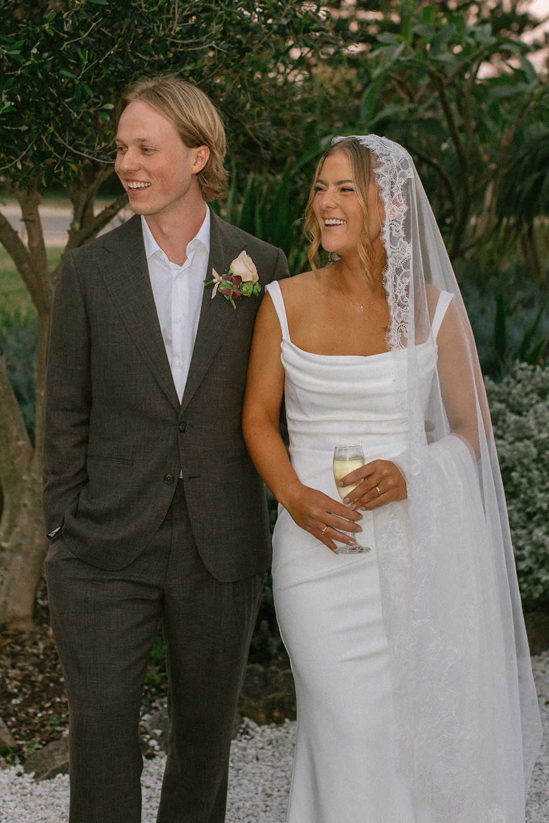Bride and groom smiling together at a wedding, surrounded by greenery.