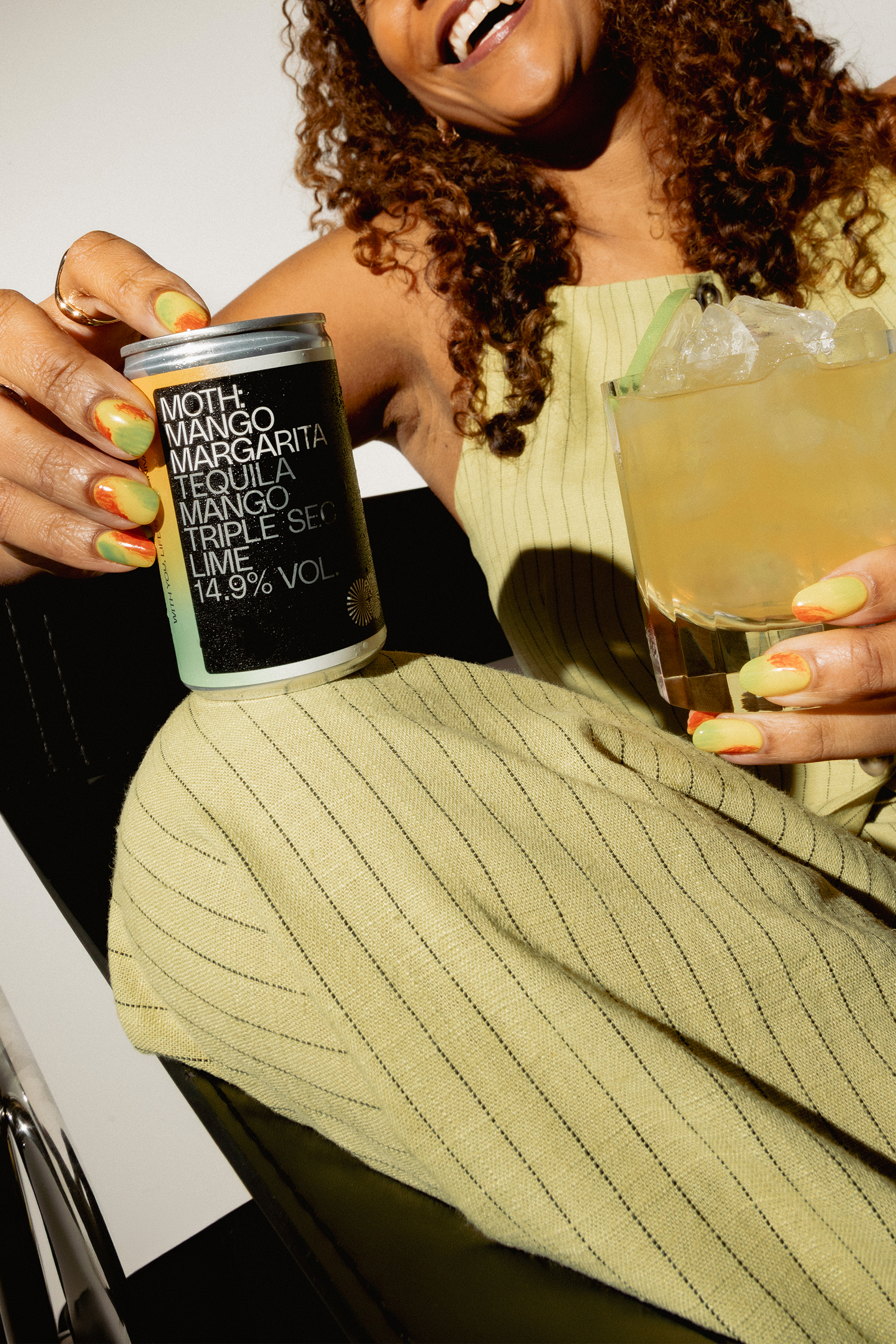Woman holding a drink and a can, smiling, wearing a striped outfit.