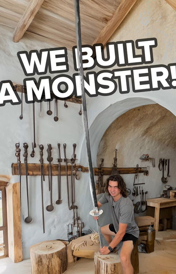 Person holding a large sword in a workshop, with tools on the wall.
