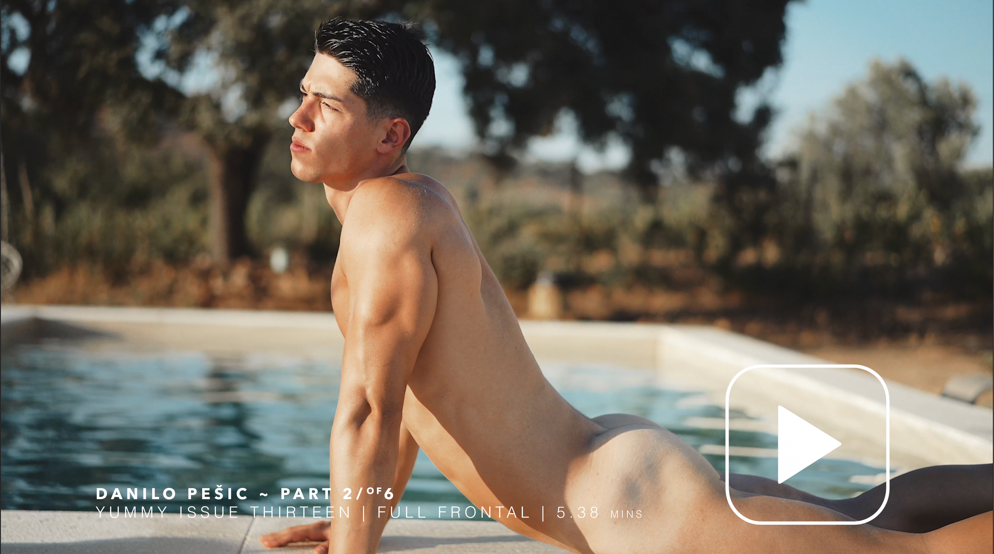 Person posing near a pool, surrounded by trees and sunlight.